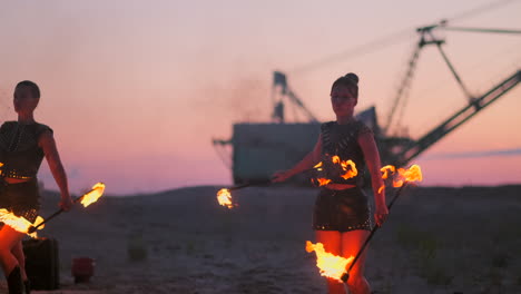 Eine-Gruppe-Von-Männern-Und-Frauen-Zeigt-Nachts-Eine-Feuershow-Auf-Dem-Sand-Vor-Dem-Hintergrund-Von-Feuer-Und-Turmdrehkränen.